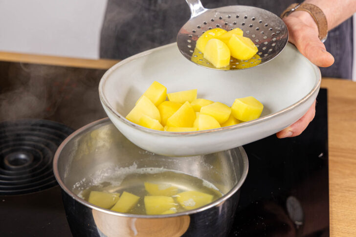 Kartoffeln aus dem Topf abschöpfen in die Auflaufform