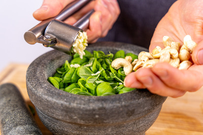 Knoblauch zum Basilikum pressen und Cashewkerne dazugeben