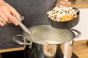 Karotten und Champignons in die Sauce geben