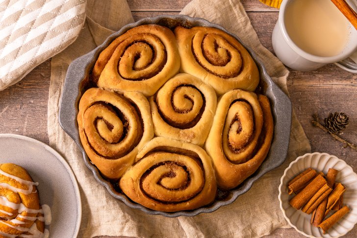 Vegane Zimtschnecken mit goldbrauner Kruste und saftiger Zimtfüllung in einer runden Backform, serviert mit Zuckerguss und Zimtstangen.
